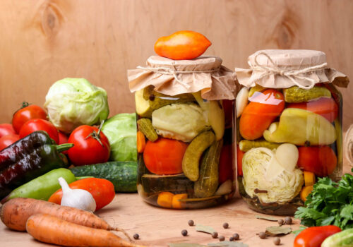 Assorted pickled vegetables in jars: cucumbers, tomatoes, cabbage, zucchini and peppers with garlic, dill and bay leaves in jars on a wooden background, horizontal photo