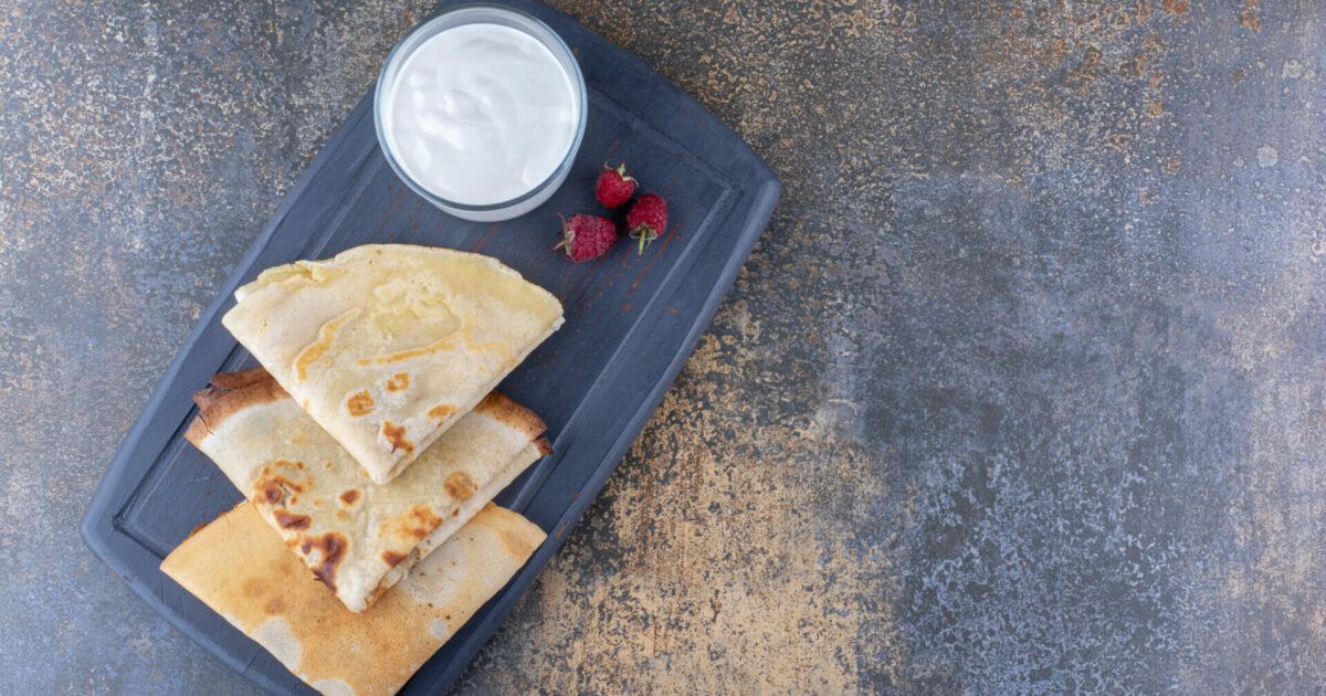 Crepes on a black platter with raspberries and a cup of milk. High quality photo