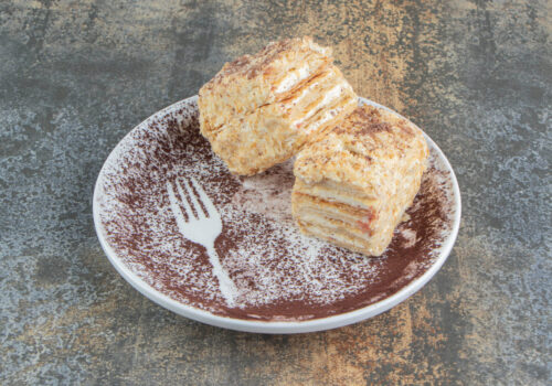 A white plate with two pieces of Napoleon cake and cocoa powder